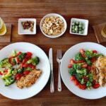 Two plates of chicken and vegetables with beer and nuts placed on the table