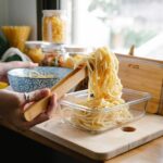 Woman putting cooked pasta noodles into a glass container