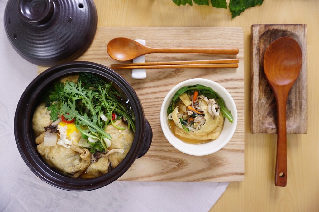 A black pot and a white small bowl filled with fish cake soup were placed on a brown wooden board