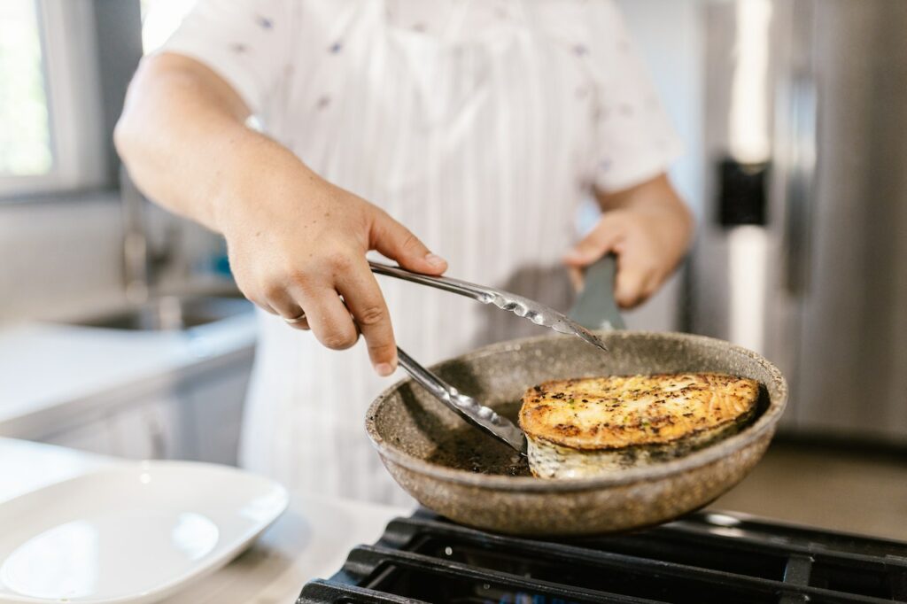 A chef cooking fish on a frying pan in the kitchen