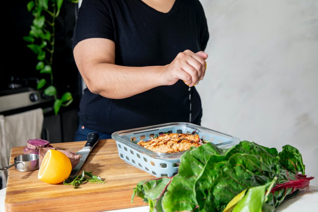 A person wearing a black shirt is squeezing fresh lemon on a slice of meat placed on a blue container on top of the brown wooden table