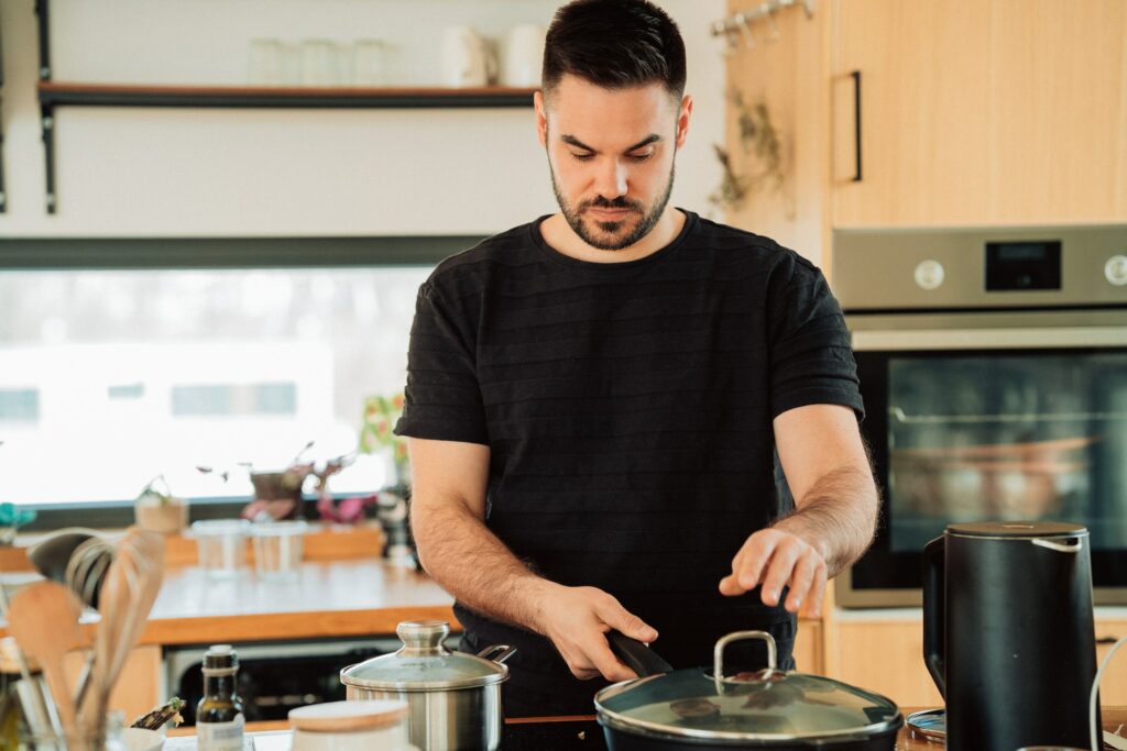 A man wearing a black shirt is cooking using a black pot with a glass cover on a black electric stove