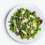 Green Asparagus with crushed nuts and celery on a white plate on top of a white table