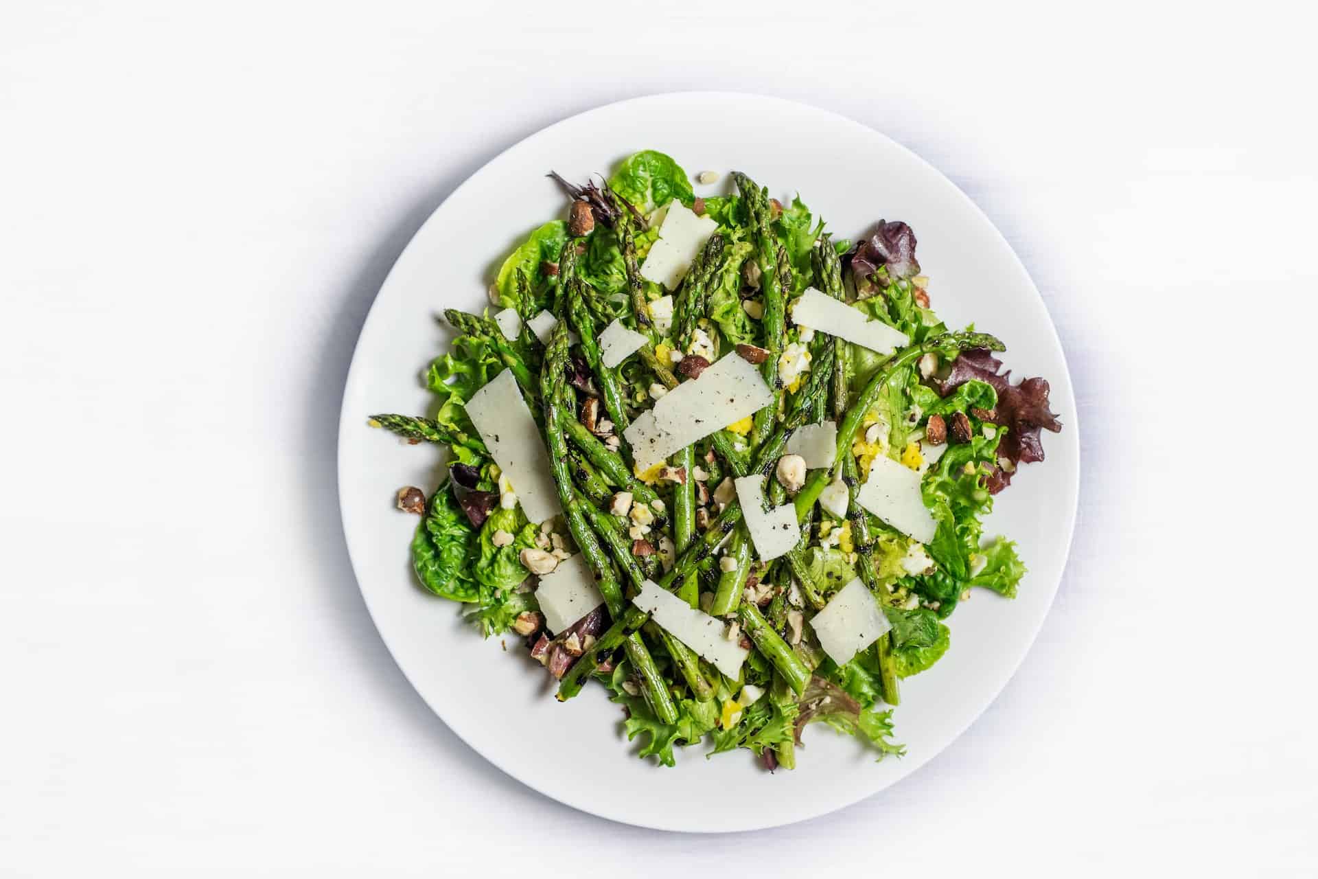 Green Asparagus with crushed nuts and celery on a white plate on top of a white table