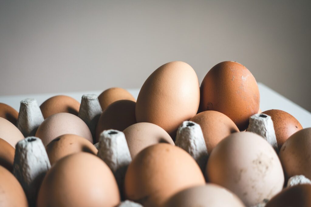 Brown eggs are placed in a brown egg carton on top of a white table
