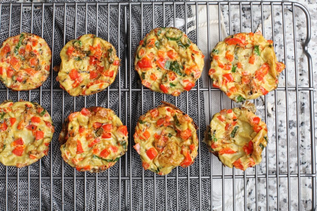Eight freshly baked egg bites place on a silver cooling rack on top of a marbled table