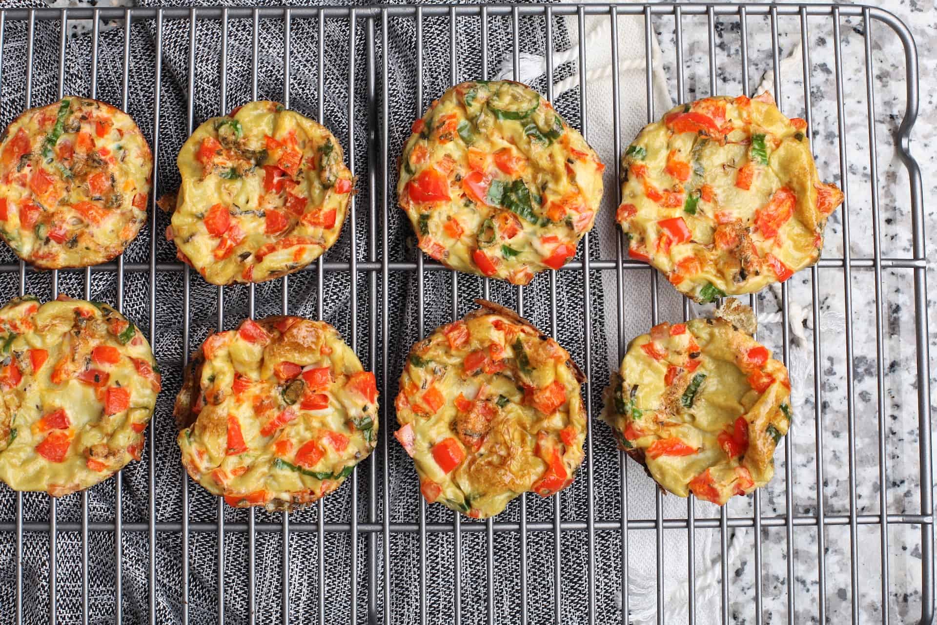 Eight freshly baked egg bites place on a silver cooling rack on top of a marbled table