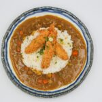 Japanese curry with sliced vegetables, white rice, and three fried Ebi tempura served in a ceramic bowl