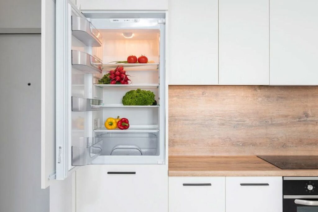Door of a refrigerator is open and shows vegetables stored inside