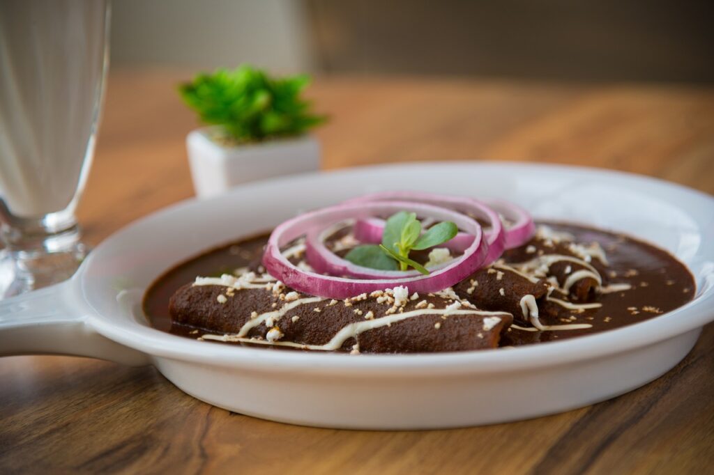 Enchilada with thick brown sauce garnished with red onions on a white serving plate on top of a brown wooden table