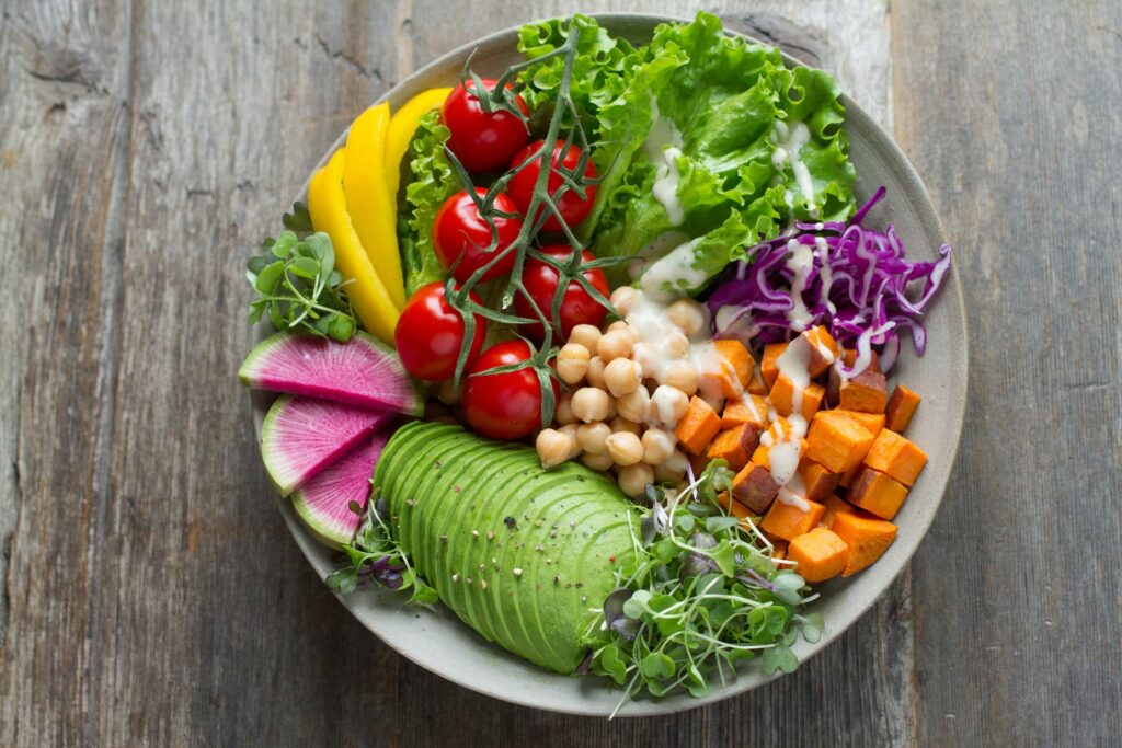 Fresh fruits and vegetable salad with white sauce on a white ceramic bowl on top of a brown wooden table