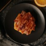 Fried bacon on top of sliced cheese is placed on a black ceramic plate on top of a black marbled table