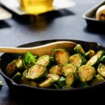 Cooked Brussels sprouts with rock salt on top and a wooden spatula inside a cast iron skillet on top of a black table