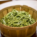 Fresh green beans inside a wooden basket on top of a brown wooden table