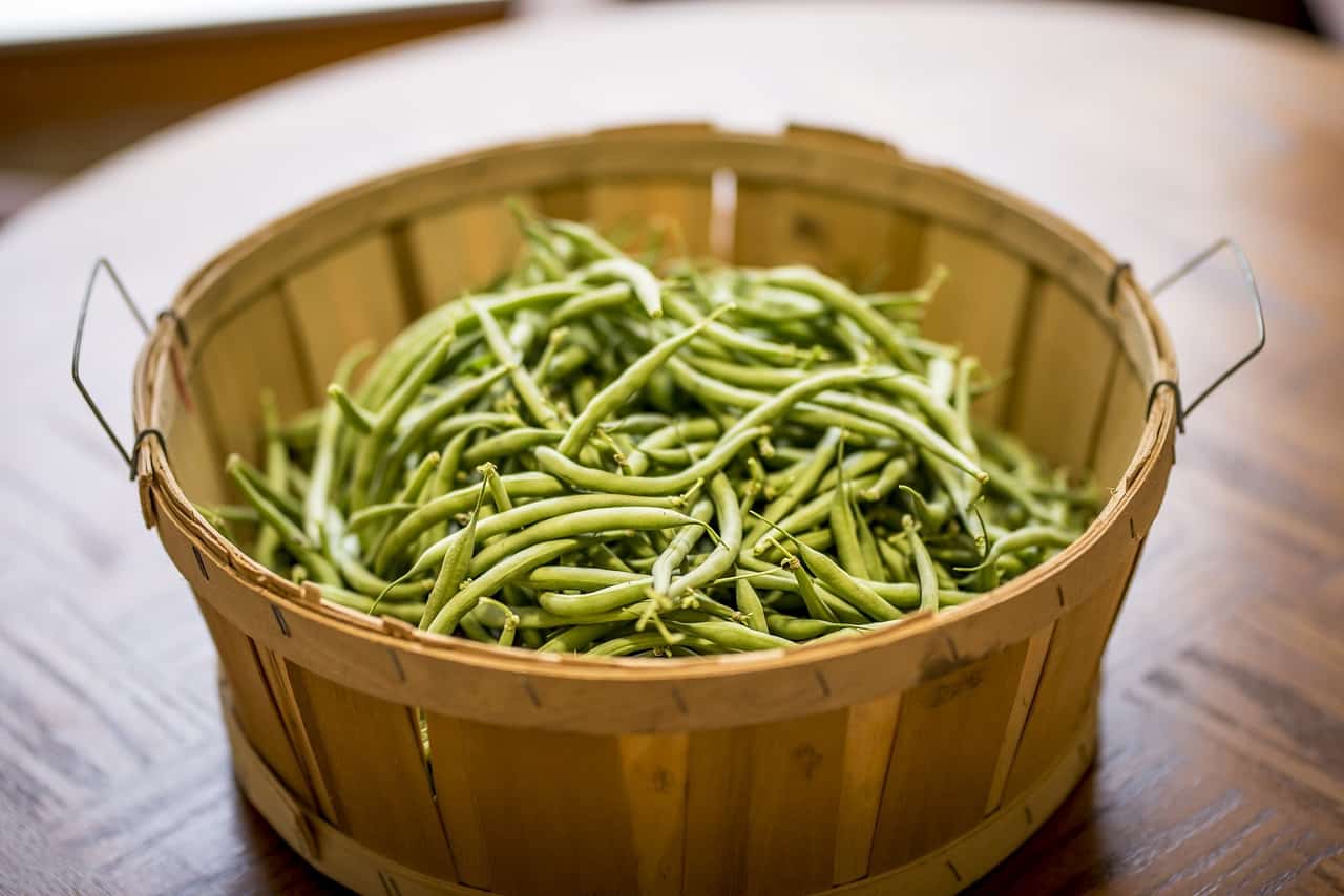 Fresh green beans inside a wooden basket on top of a brown wooden table