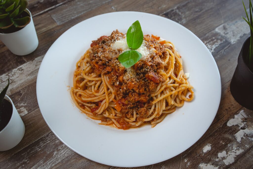 Spaghetti garnished with parmesan cheese and fresh basil on a white ceramic plate on top of a brown wooden table