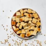 Sliced tofu with brown sauce on a white plate on top of a white surface
