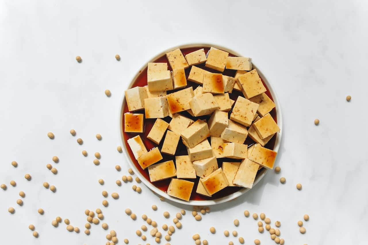 Sliced tofu with brown sauce on a white plate on top of a white surface