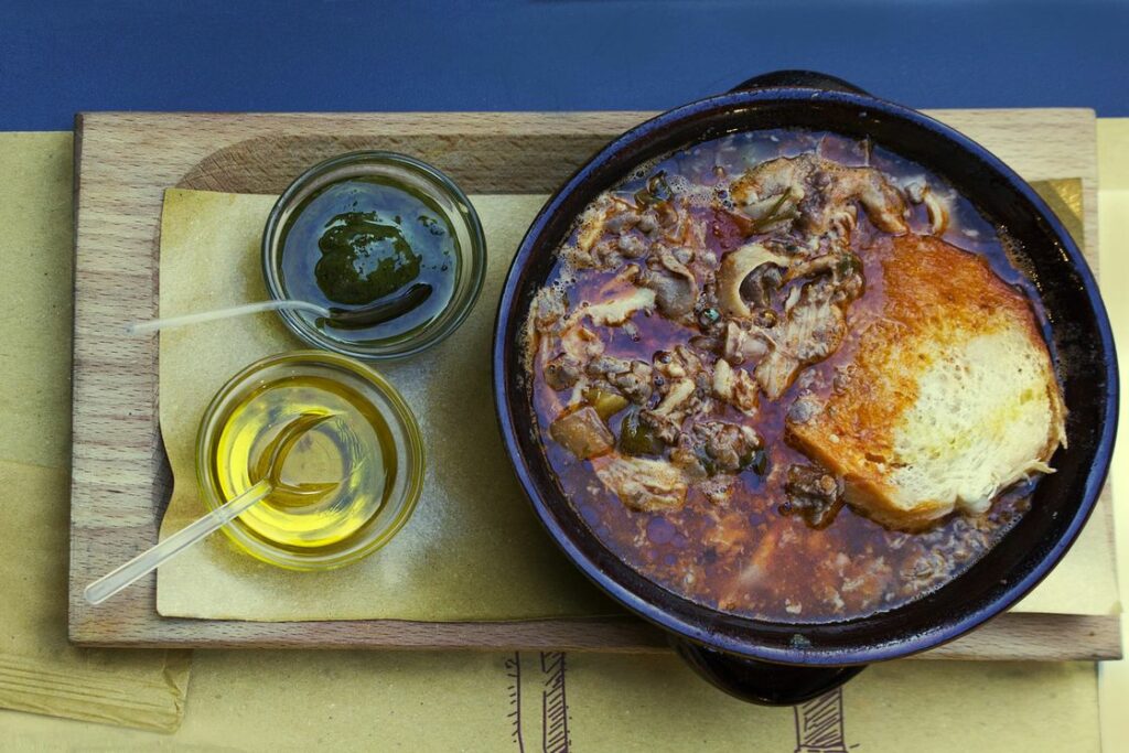 Stewed meat in a cast iron pan with a side of olive oil and chimichurri sauce on a wooden tray