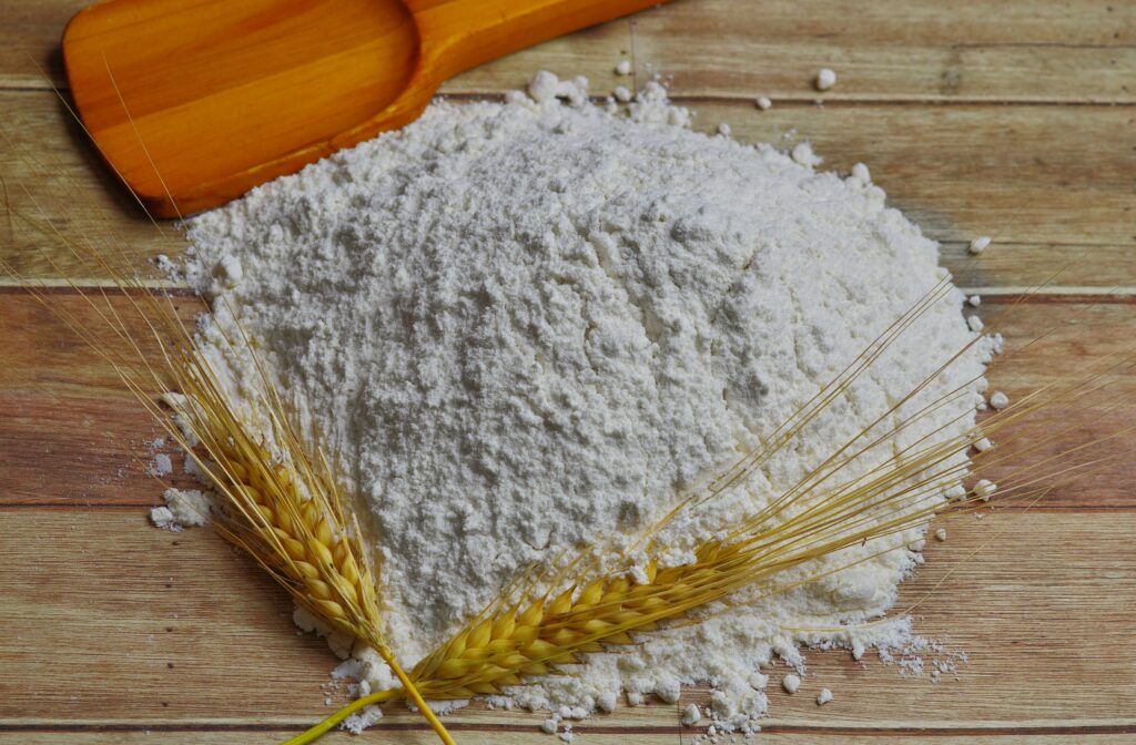 A flour along with a grain and a wooden spoon on a table