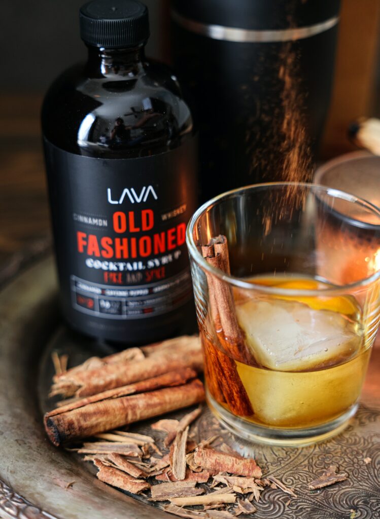 A bottle of cinnamon cocktail syrup with a glass of cocktail