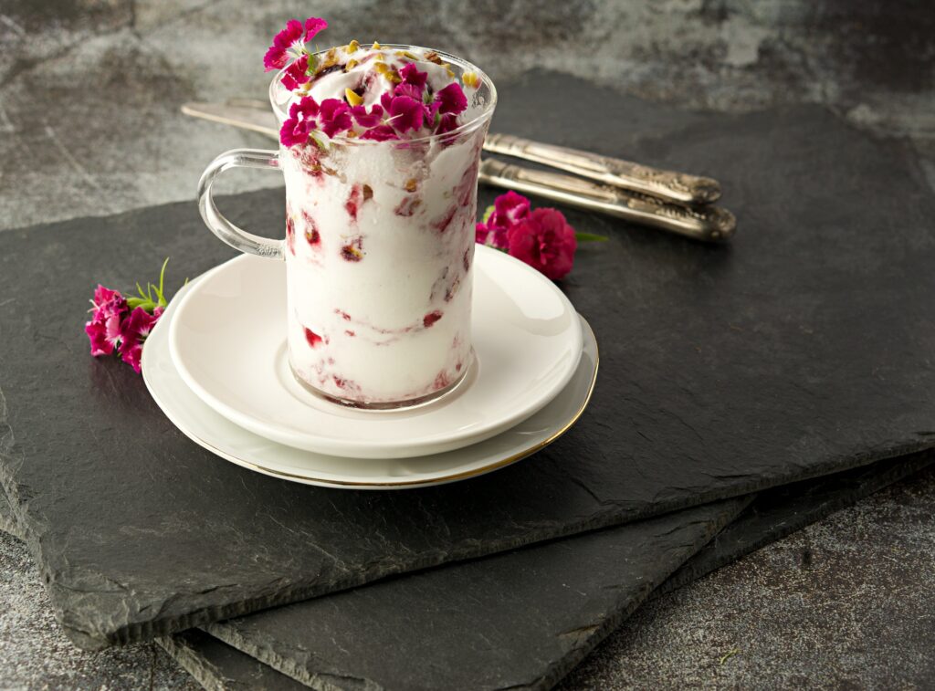A glass mug of mascarpone with pink flowers in small plates and utensils