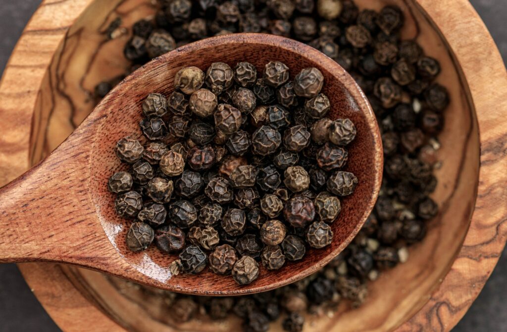 An image of black pepper in wooden bowl and spoon