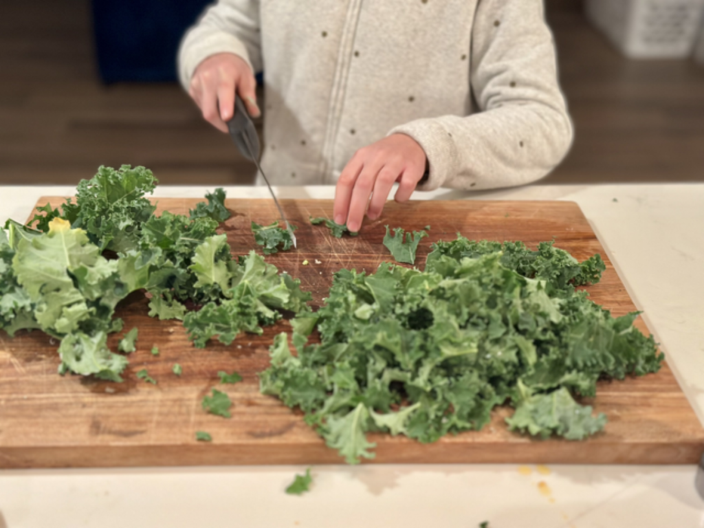 A person chopping kale on a wooden cutting board