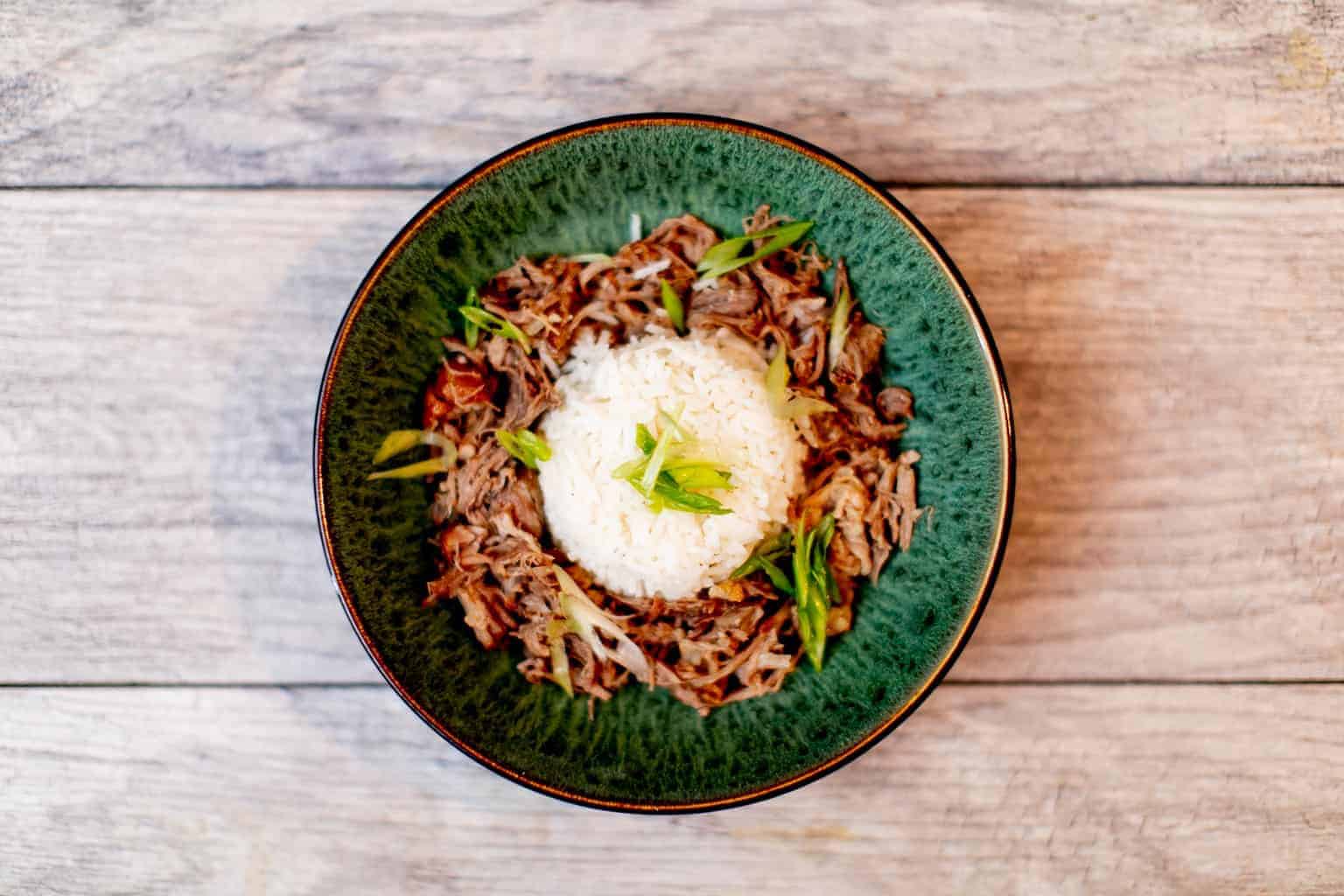 Shredded beef with rice topped with green onions in a green bowl