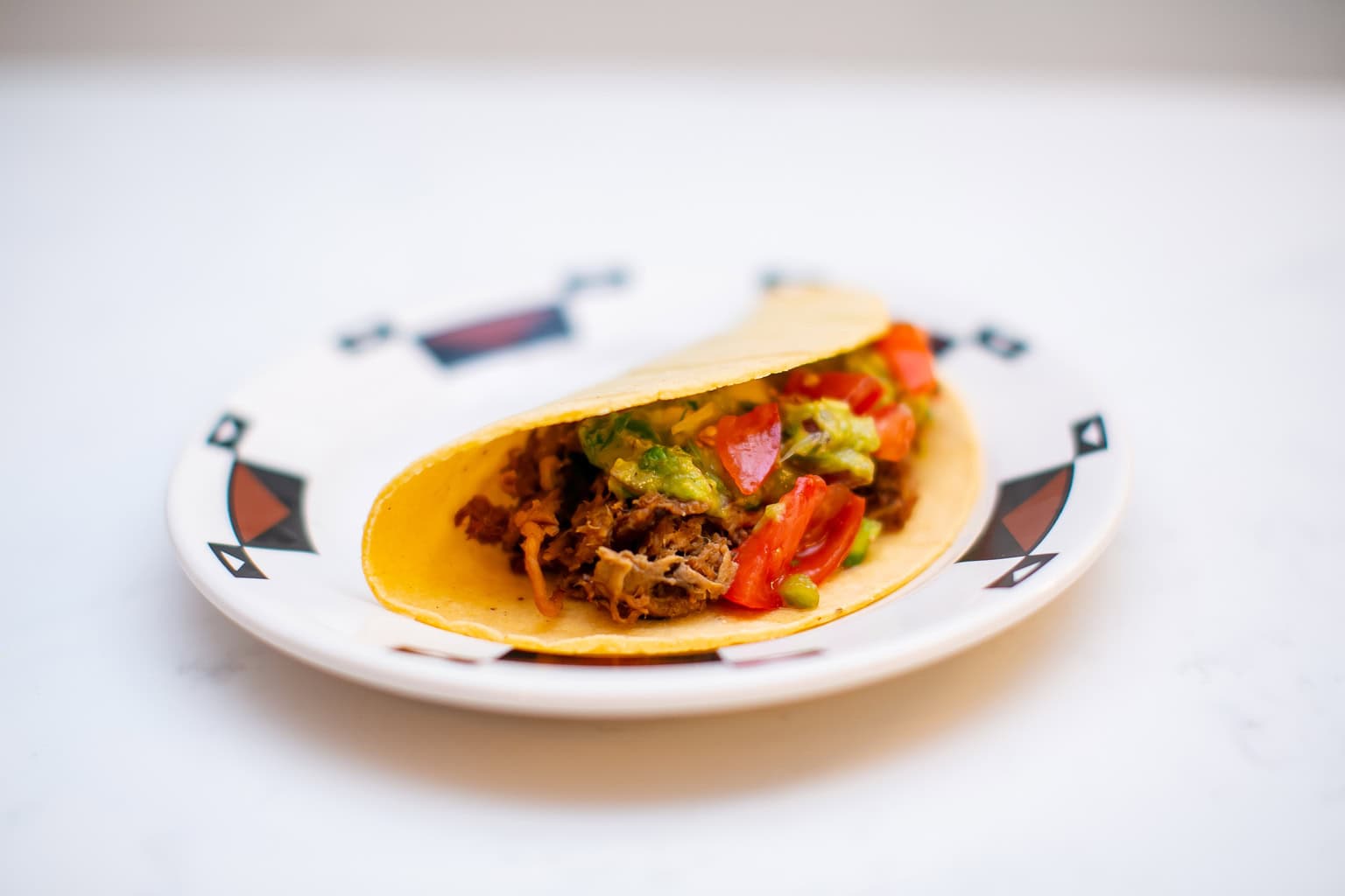 Taco filled with seasoned beef, topped with fresh guacamole and diced tomatoes