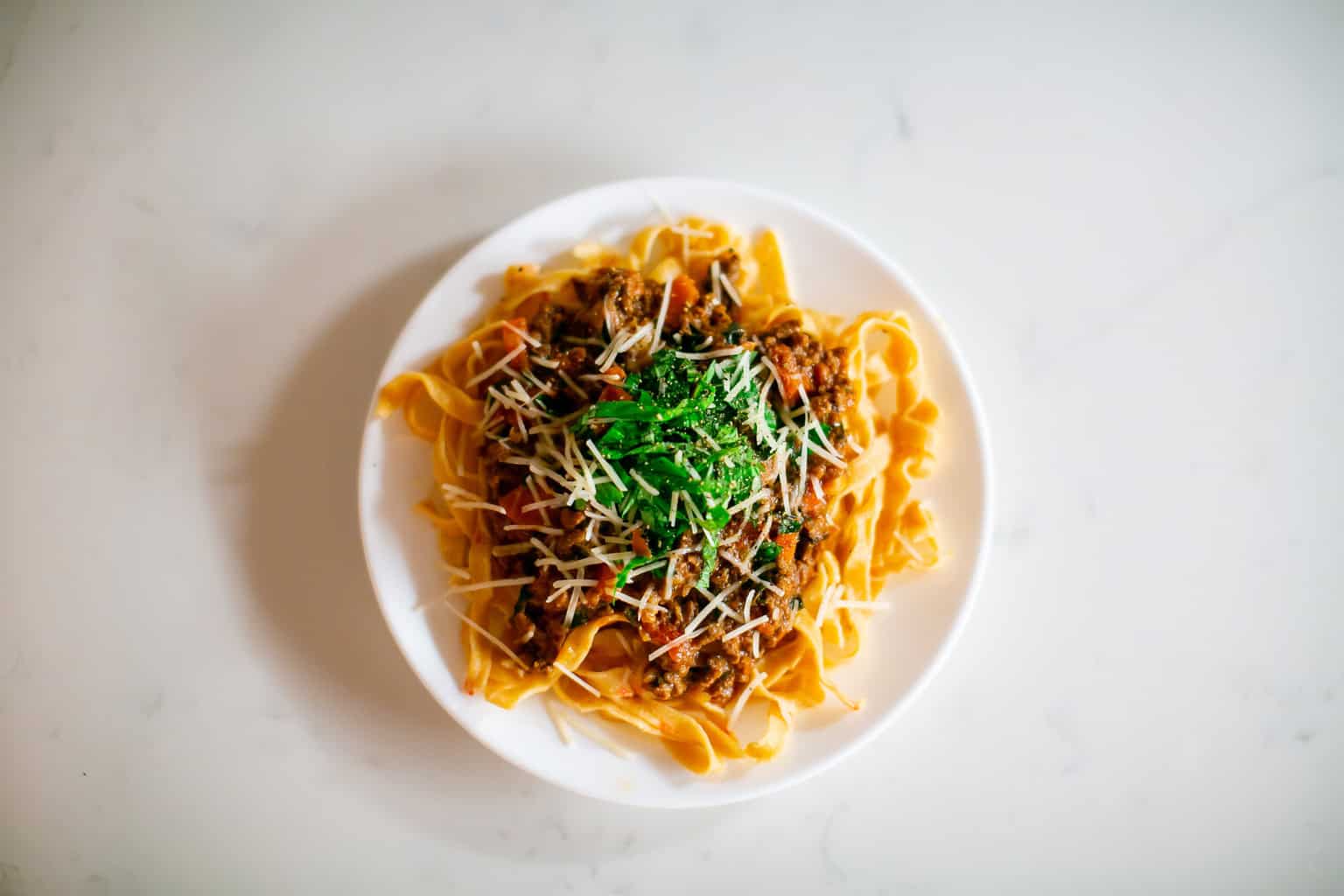 Fettuccine pasta with hearty meat sauce, topped with grated parmesan and fresh herbs