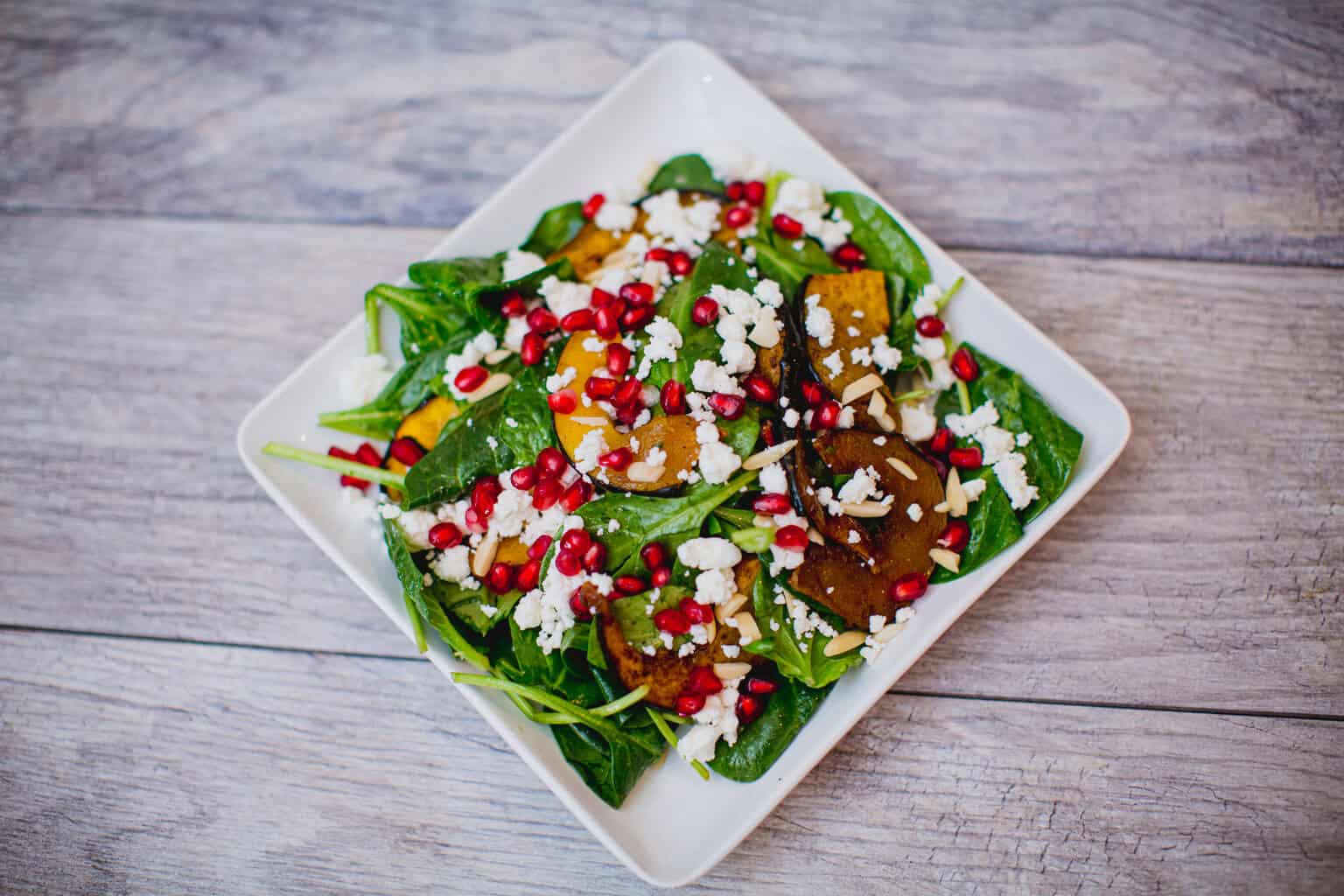 A fresh spinach salad with roasted squash, pomegranate seeds, and feta cheese