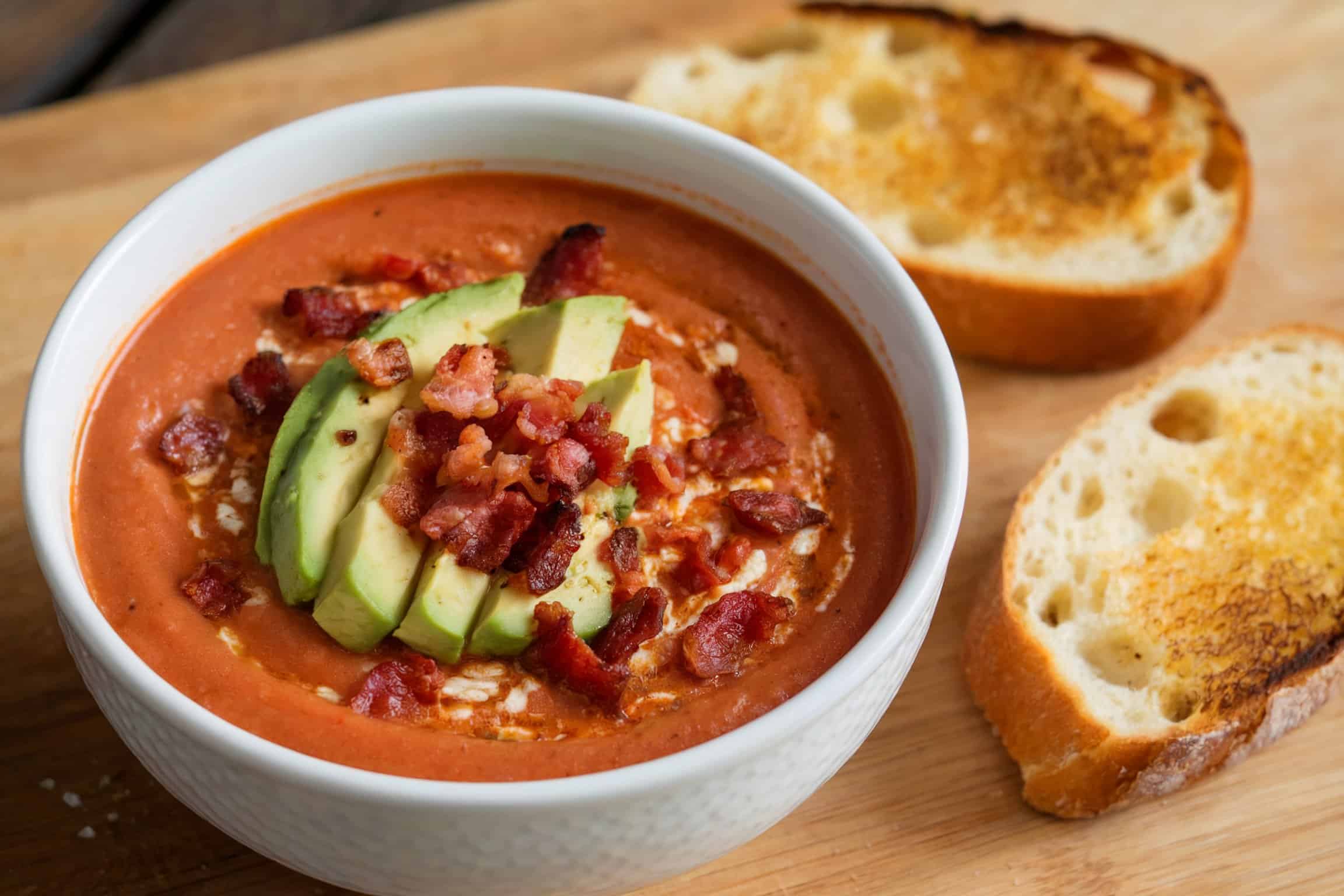 A bowl of cream tomato soup with bacon and avocado