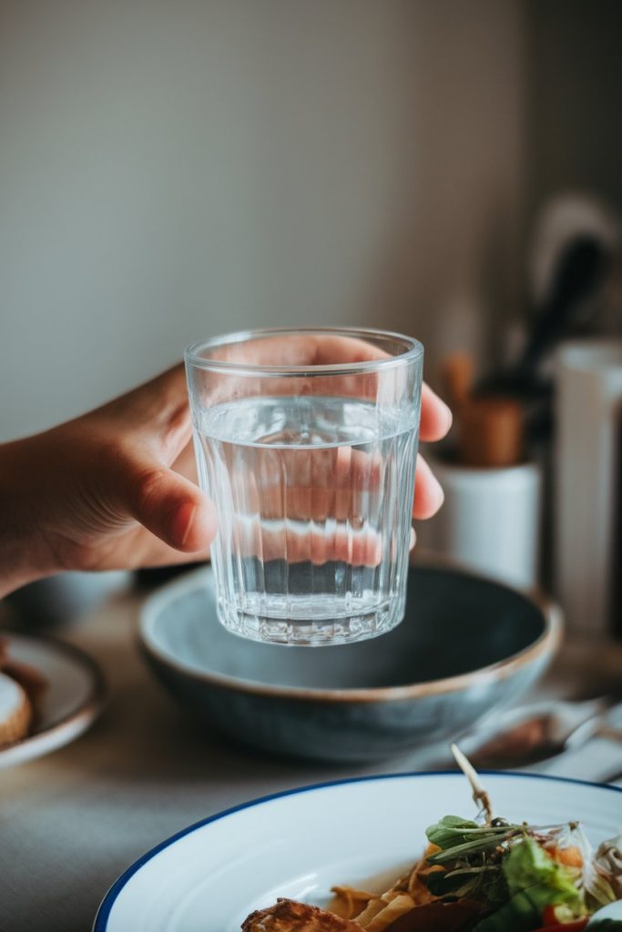 Close-up of a hand holding a glass of water next to a plate with food