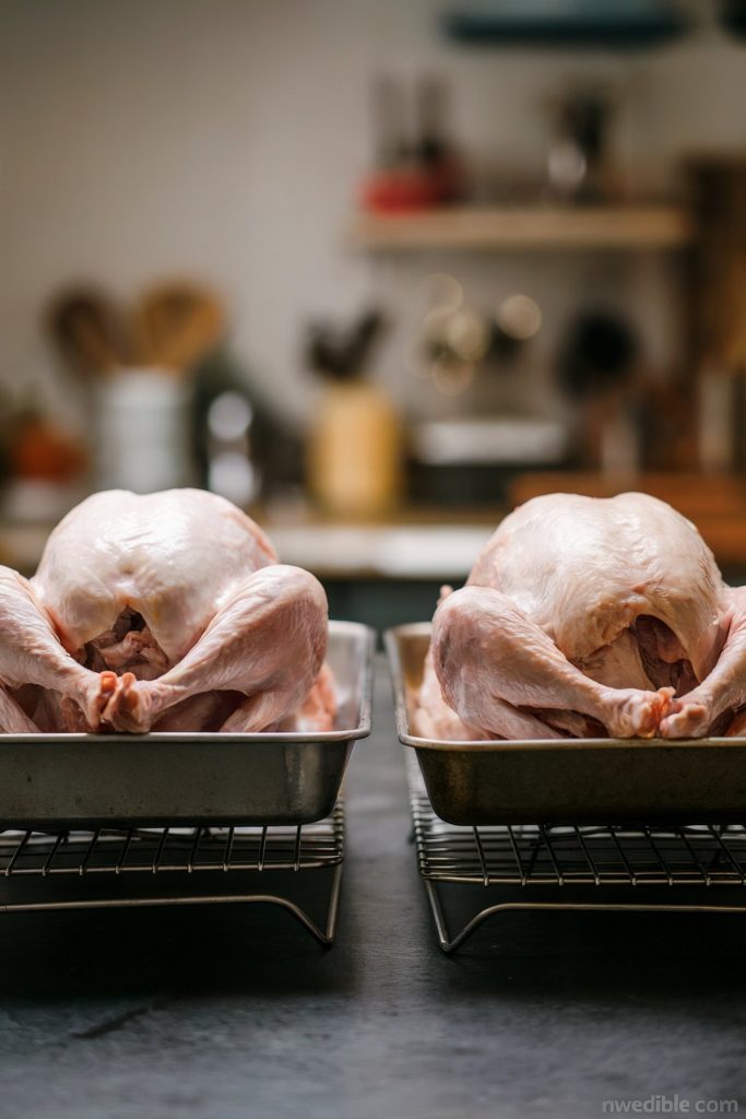 A whole, raw turkey is placed in a metal roasting pan on a shelf inside a refrigerator