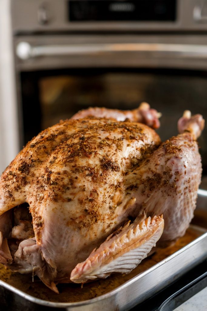 A raw whole turkey resting on a wooden cutting board in a well-lit kitchen, with a lemon and a white kitchen towel nearby, ready for preparation.