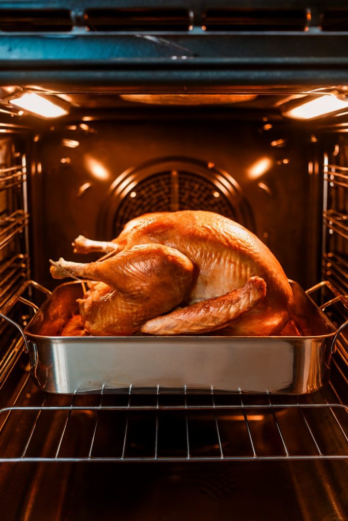 A fully roasted turkey with golden brown, crispy skin sitting in a roasting pan inside an oven