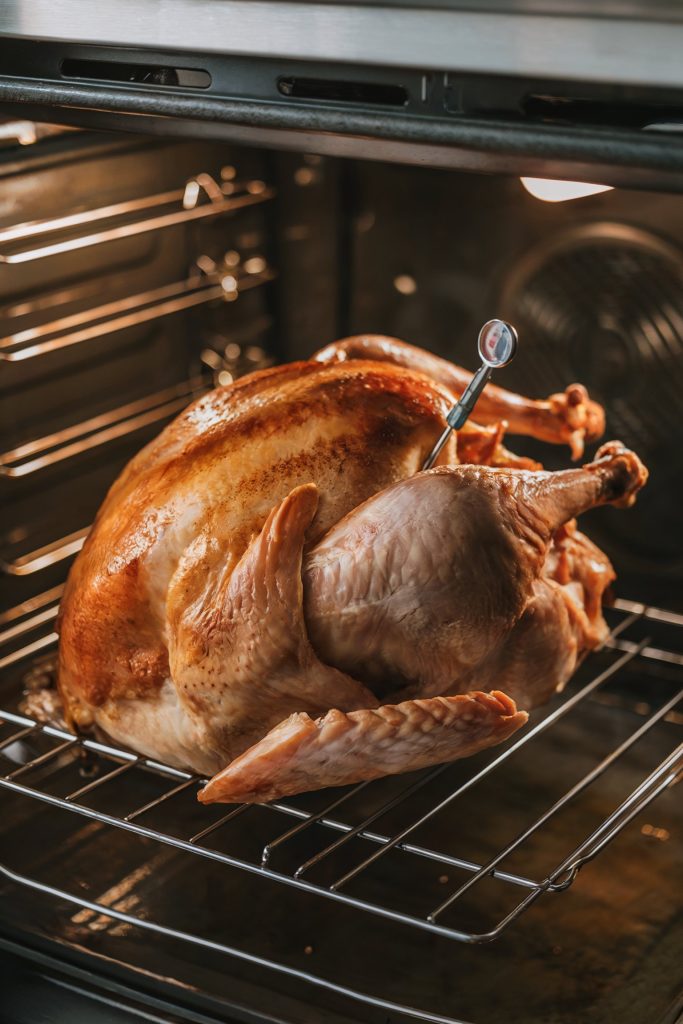 A partially cooked turkey in an oven with a meat thermometer inserted into the thickest part of the breast
