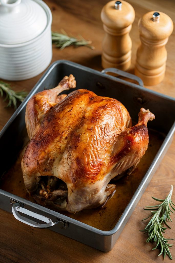 A cooked whole turkey on a pan with salt and pepper bottles beside it