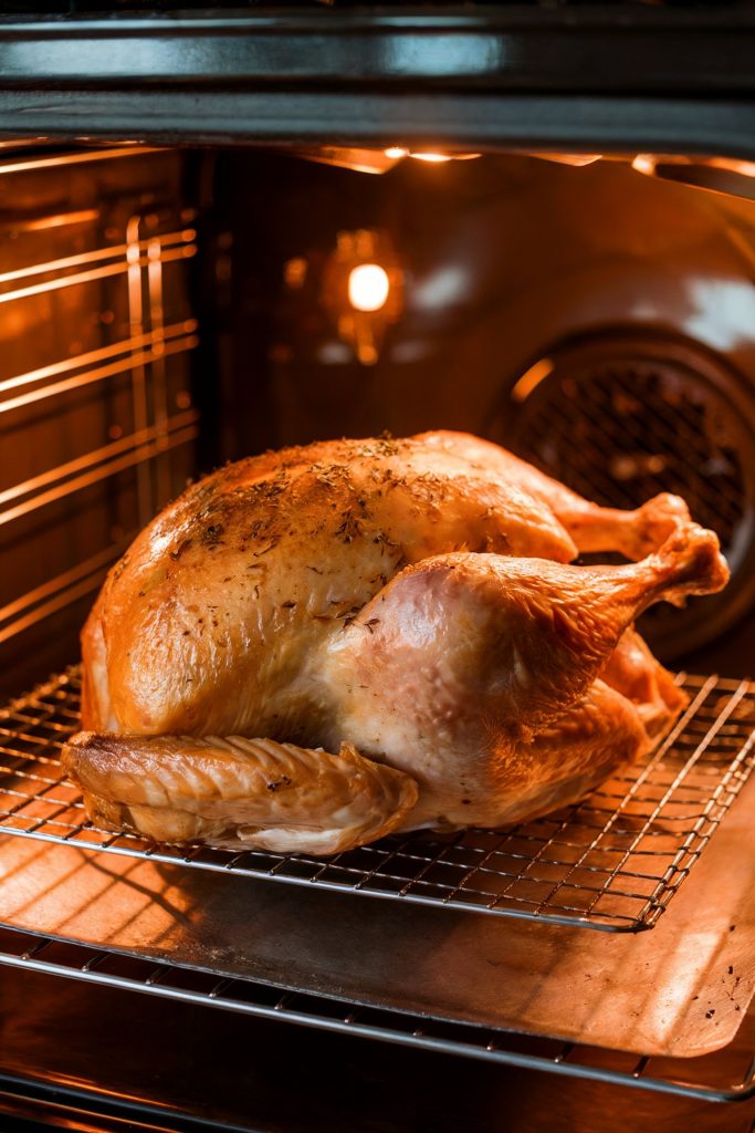 A fully cooked turkey with crispy, golden skin rests in a roasting pan inside an oven