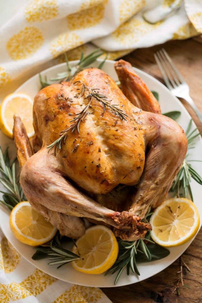 A glazed turkey on a whit plate with lemons and herb