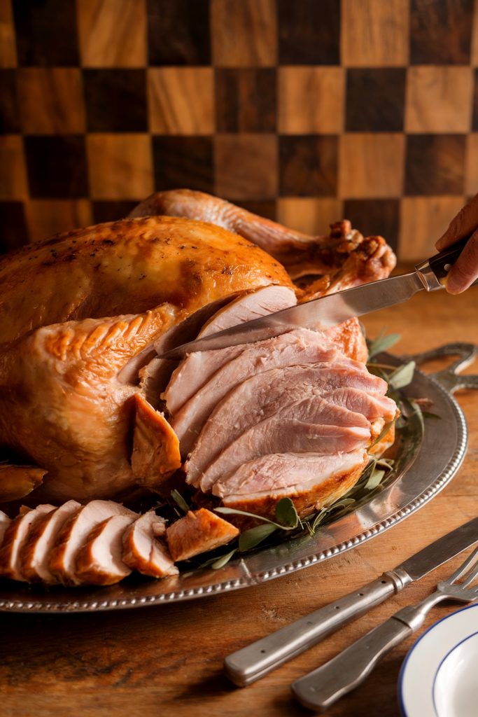 A hand cutting the turkey using a knife with some slices already
