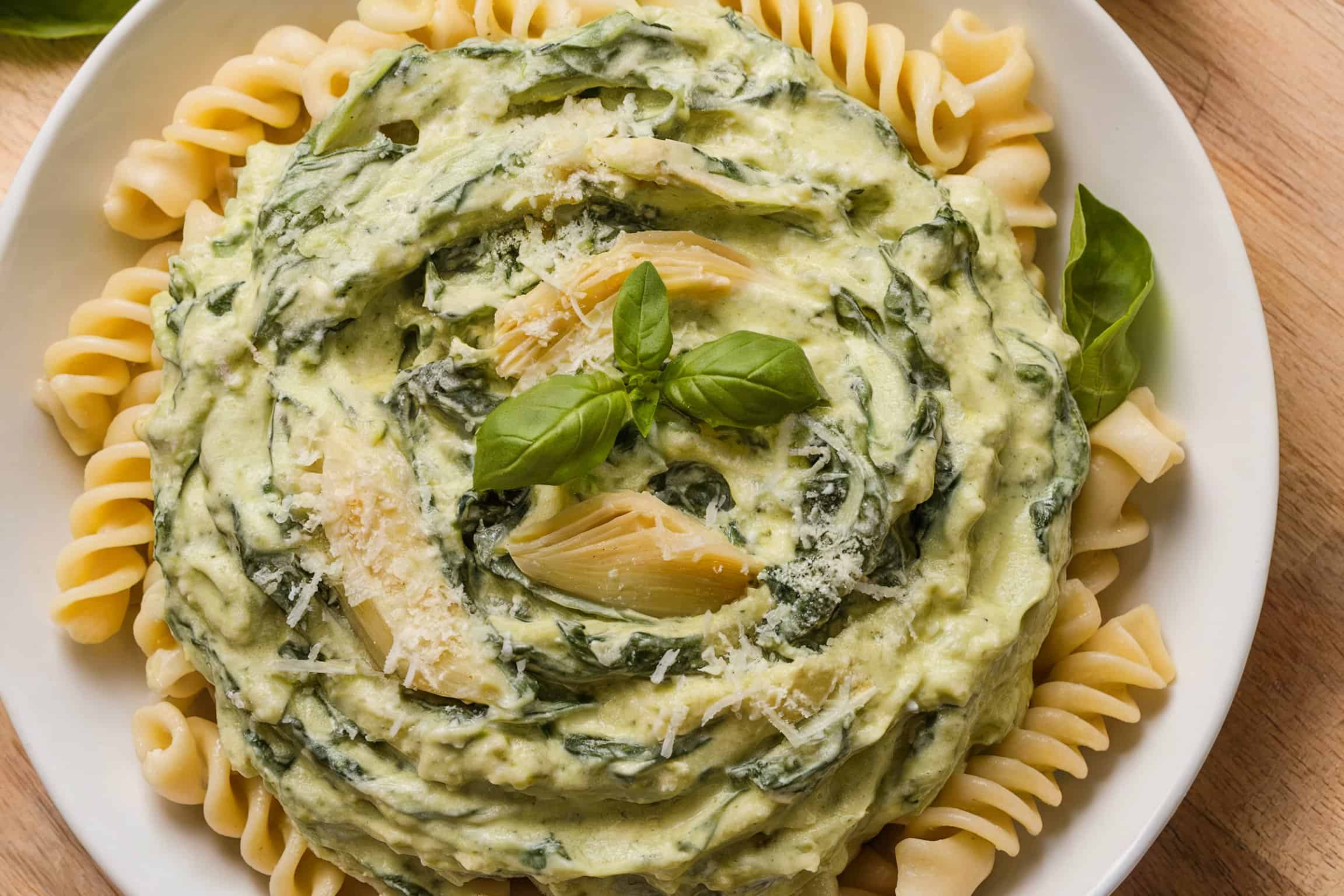 A plate of pasta with a creamy spinach and artichoke dip sauce