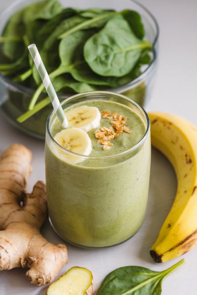 A green smoothie with banana, ginger, and spinach beside it