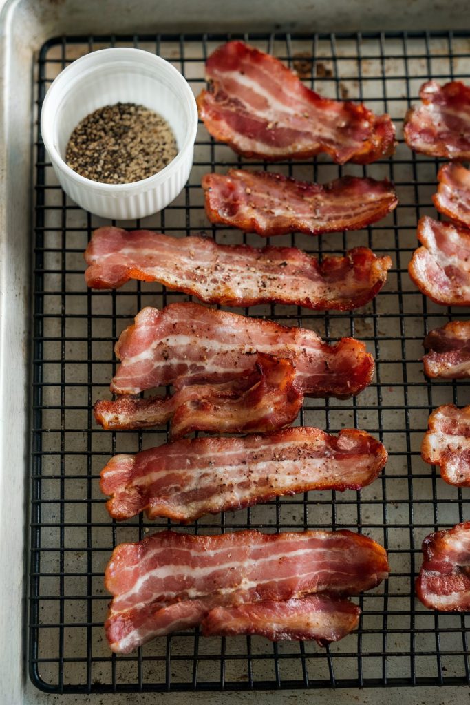 Bacon strips sprinkled with ground black pepper with a bowl of it  on the side