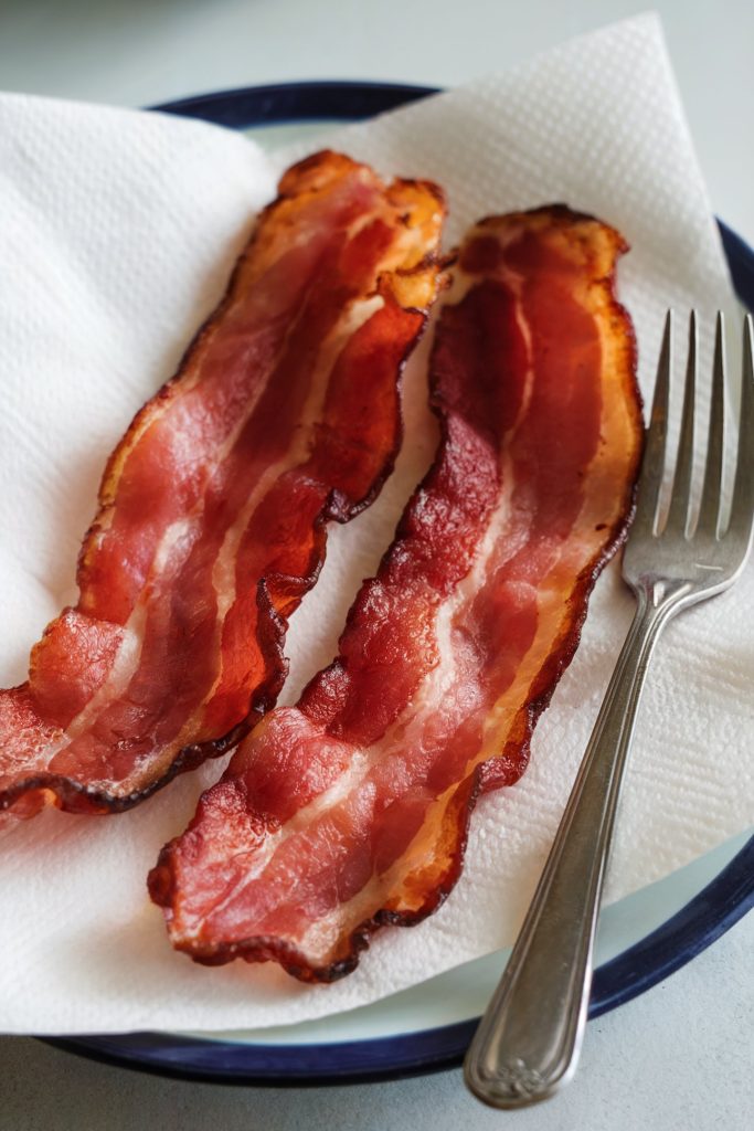 Two pieces of bacon strips and a fork placed over a tissue paper