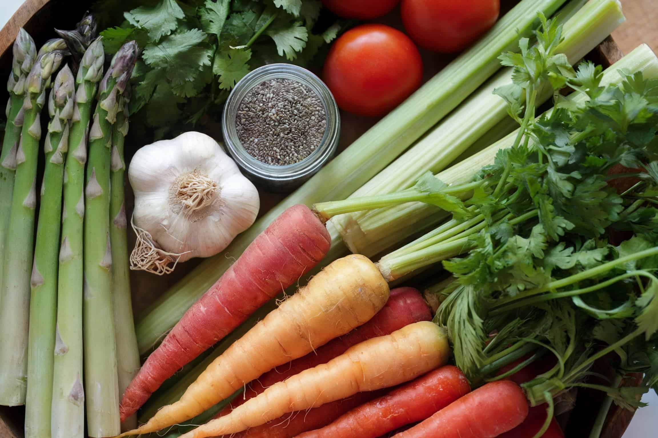 Asparagus, carrots, garlic, tomatoes. chia seeds and some leafy greens on a table