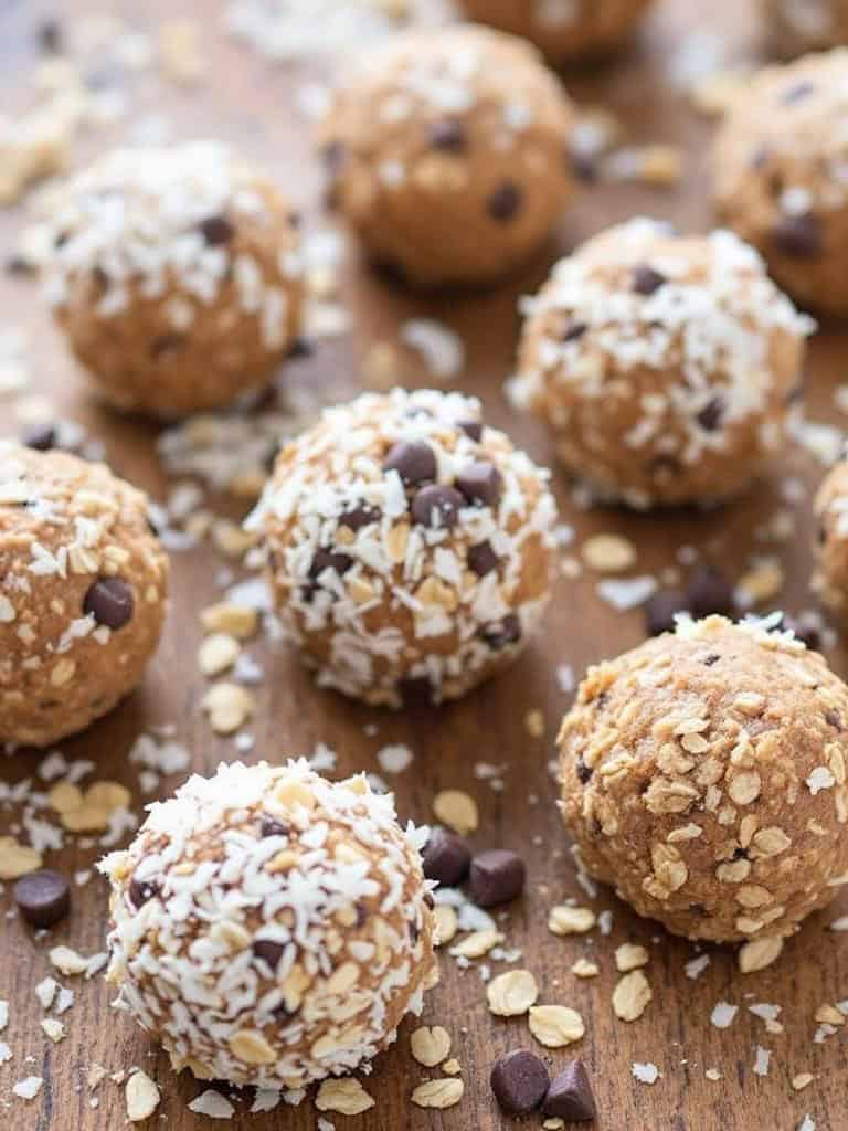 A variety of oatmeal energy balls with chocolate chips and oats scattered on a wooden surface.