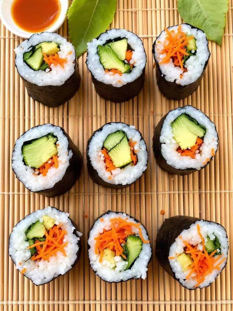 A platter of veggie sushi rolls with colorful vegetables and dipping sauce.