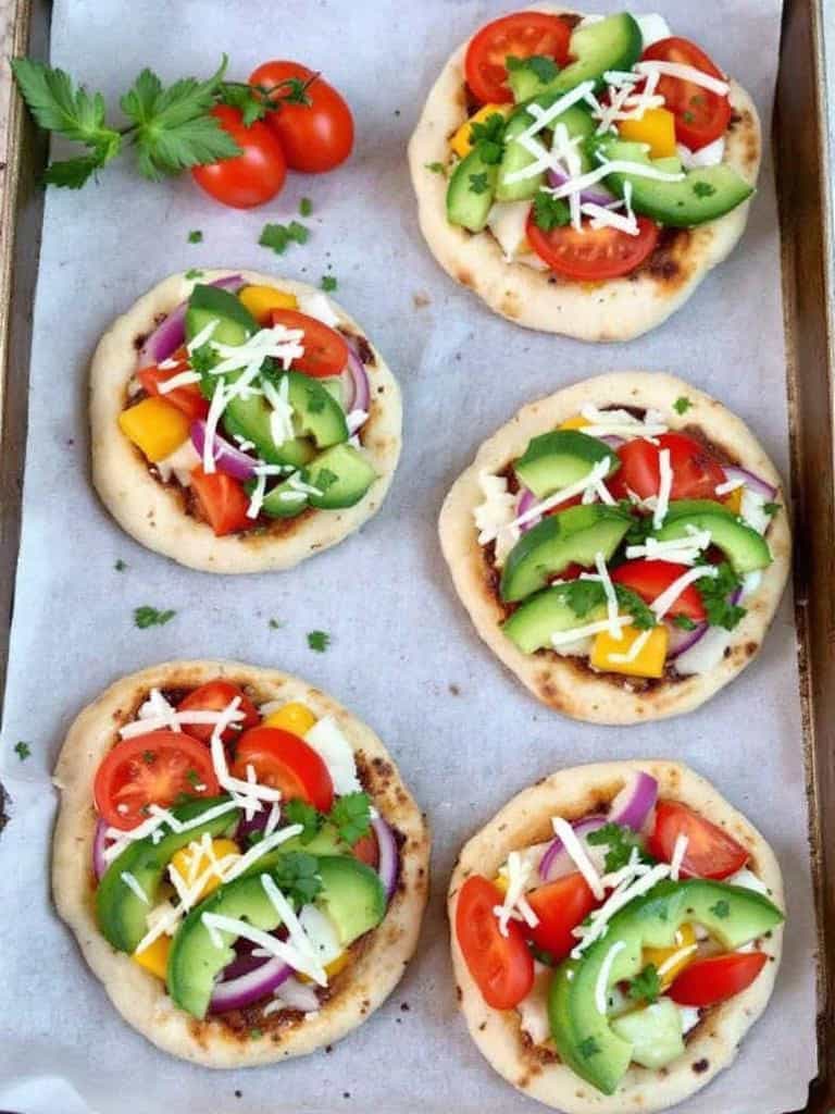 Mini pita pizzas topped with tomatoes, cheese, and herbs on a baking tray.